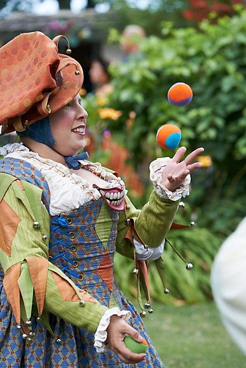 Photo by Ivan Phillips of a 16th-century jester in a blue, green, red, and orange brocade-and-silk motley, juggling three multicolored juggling balls.