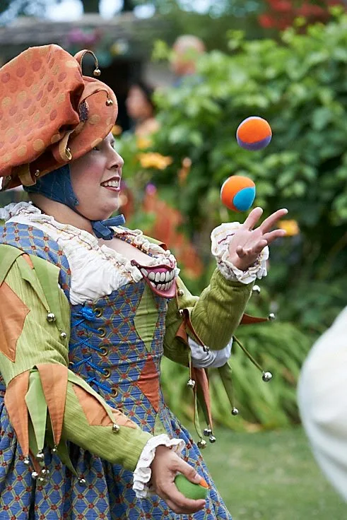 Photo by Ivan Phillips of a 16th-century jester in a blue, green, red, and orange brocade-and-silk motley, juggling three multicolored juggling balls.